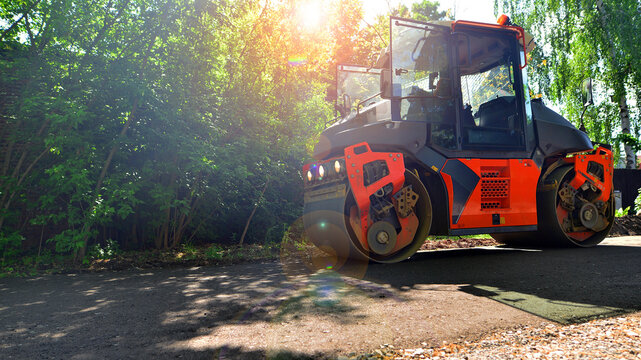 An orange road roller compactor freshly laid asphalt on a new suburban street during daytime.