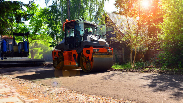 An orange road roller compactor freshly laid asphalt on a new suburban street during daytime.