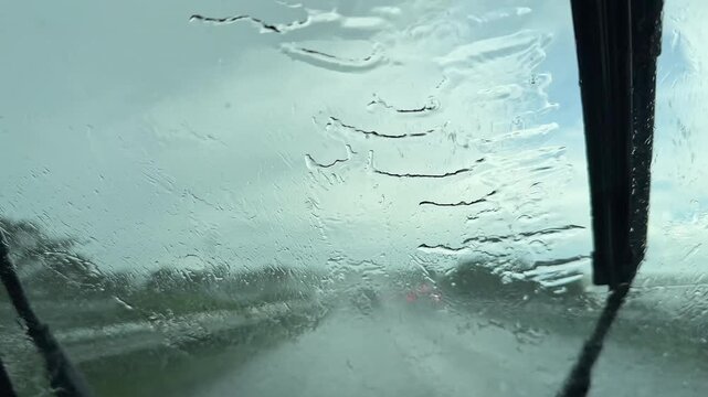Rain covers the windshield as a driver navigates the highway. The visibility is low due to the downpour. The wipers move back and forth, trying to clear the glass.