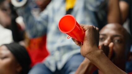Close side view of passionate male football fan blowing red vuvuzela in stadium stands during intense live soccer match. © DC Studio