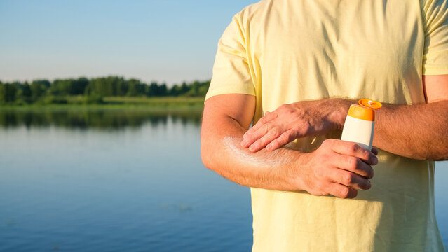 Sunscreen cream applied to arm in outdoor lakeside setting. Concept: SPF skincare, UV prevention, summer lifestyle