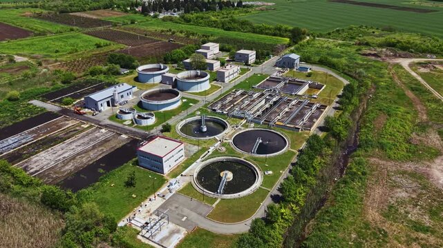Aerial sewage treatment plant captured over verdant landscape with circular clarifiers and aeration basins emphasis on renewable biogas potential, drone