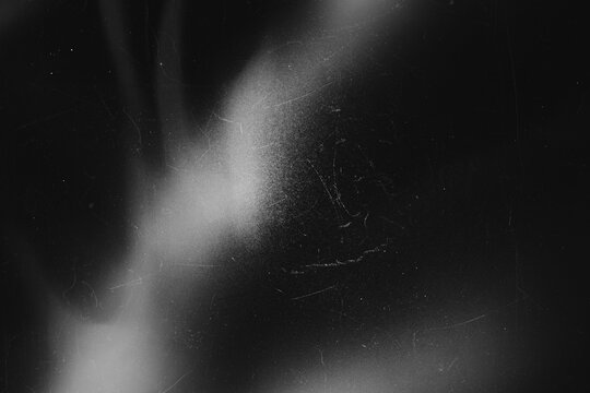 Dark grunge film dust and scratch texture overlay with soft light bloom on black background