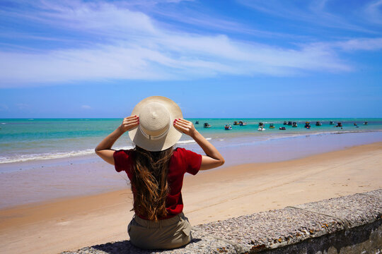 Back view of woman sitting on wall enjoying sight of natural swimming pools with jangadas rafts in Joao Pessoa, Brazil