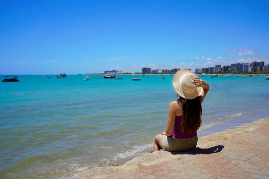 Holidays in Maceio, Brazil. Young woman sitting enjoying view towards natural swimming pools of Pajucara, Maceio, Brazil.