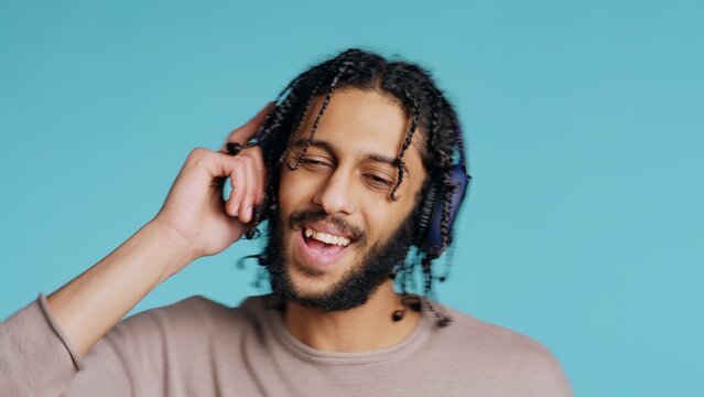 Joyous Middle Eastern man listening music, having fun, dancing on rhythm, enjoying leisure time. Upbeat BIPOC person wearing headphones, doing funky movements, studio background, camera B