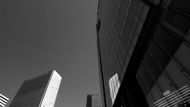 ビルの谷間を見上げながら街中を移動するモノクロ映像　不穏な経済と不動産のイメージ