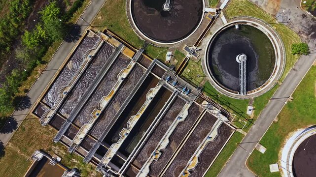 Aerial wastewater treatment plant tanks clarifiers visible rectangular aeration basins circular settling pools overhead view showing dark sludge layers access