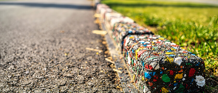 Dense vivid multicolored recycled plastic curb stones in bright daylight. Sustainable textured edging separating asphalt road and green grass