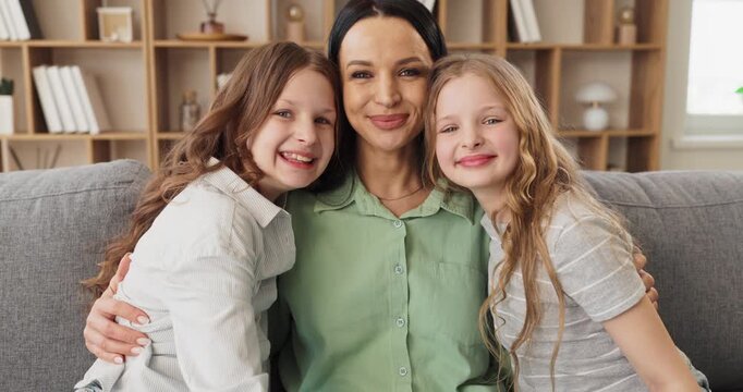 Mother daughters portrait smiling together love bonding happiness. Warm embrace on cozy sofa at home highlights caring parenting, joyful smiles, and affection. Concept shows family love bond.