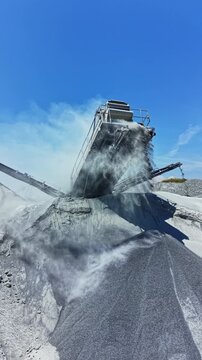 Granite quarry operates machinery to crush stones and move materials. Dust rises in the air as equipment works under a bright blue sky. Heavy machinery plays a key role in production.