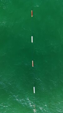 Two wooden markers and one white marker float on the blue water. They are likely set up to guide boats or swimmers in this area.