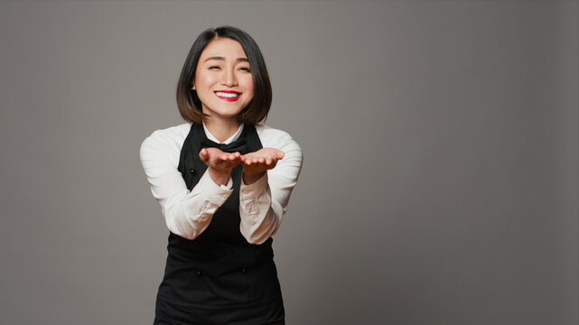 Cute flirty waitress blowing air kisses in front of camera, acting romantic with sweet gesture, asian restaurant employee posing with a kissy facial expression, catering industry.