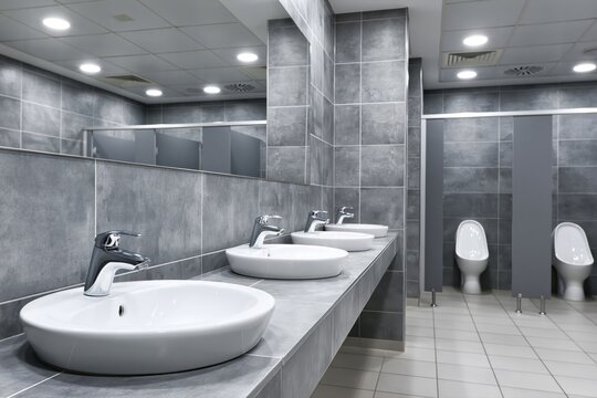 Modern public restroom with multiple sinks, urinals, and tiled walls, reflecting a clean and contemporary design.
