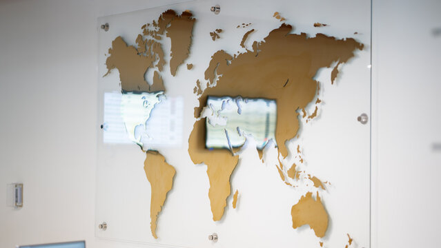 Golden world map wall art on glass panel mounted in modern office interior wall