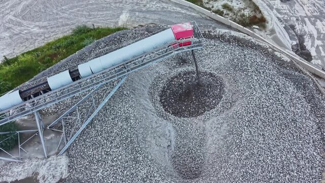 Aerial feed conveyor over fish pond captures dense flock of gulls swirling around feed outlet, industrial platform and pipe, water surface churned by activity,