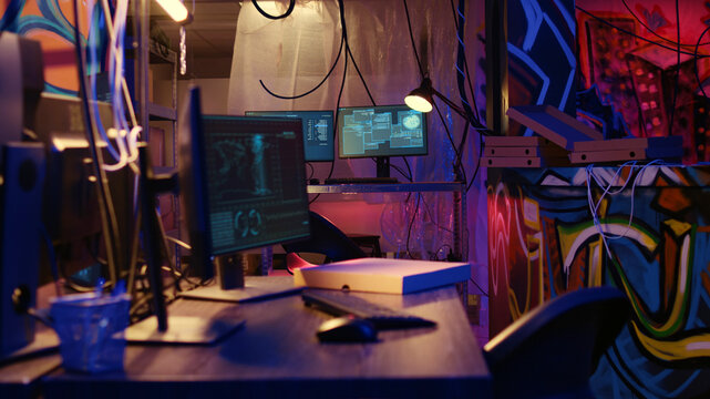 Dolly out shot of empty messy hackers base of operations with neon lights and graffiti drawings sprayed on walls, Ghetto hideout used by criminals to commit illegal activities using computers.