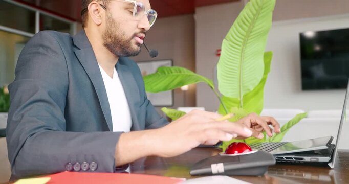 Businessman typing on laptop with headset in modern office