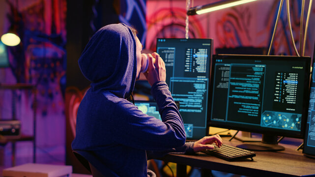 Hacker drinking coffee at underground bunker desk while using network vulnerabilities to exploit servers, trying to break computer systems at night, Lone wolf cybercriminal breaching networks.