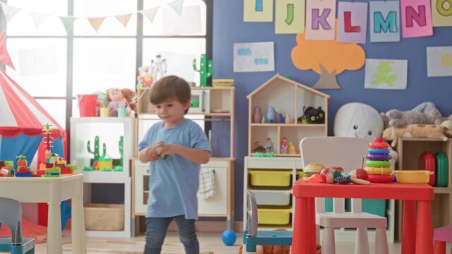 Little boy stacks colorful rings and reaches for a toy on a red table in a preschool classroom building; curious playful.