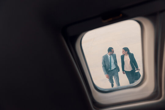 Two confident business executives walking and talking on airport tarmac viewed through a private jet window with natural copy space ideal for corporate travel and luxury aviation themes