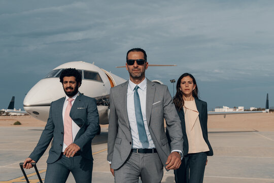 Confident Middle Eastern business team of three executives walking away from a private jet on an airport tarmac under soft overcast sky ideal for luxury aviation and corporate leadership concepts