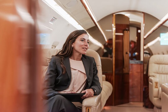 Confident businesswoman holding a tablet while seated in a luxury private jet cabin with warm natural light ideal for executive travel women leadership and premium aviation concepts
