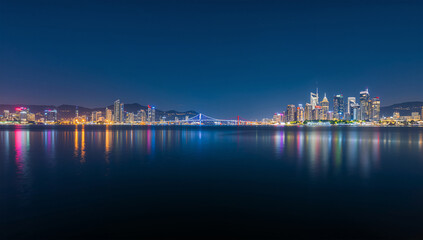 Fototapeta premium 夜の都市湾で高層ビルの光が水面に映るパノラマ風景