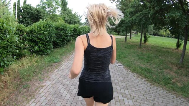 A woman in exercise clothes is seen running in a park at sundown to demonstrate a healthy lifestyle. fit girl jogger is seen running on a rural roadway while engaging in cardiovascular workout outside