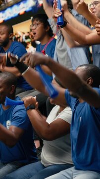 Vertical Video Black football supporters leading blue stadium chants with drum and megaphone, surrounded by passionate fans during live soccer match, sports fans with face paint and scarves, stadium