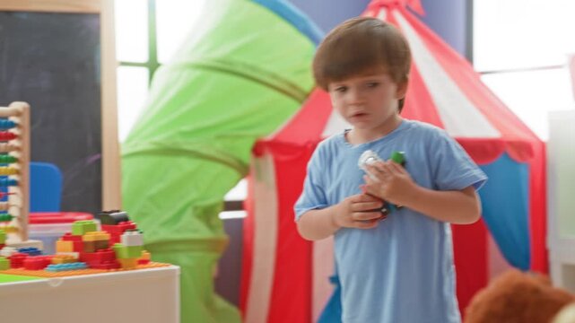Boy with hand on white chair rearranges colorful ring stacker toy in a playroom inside a building; playful curiosity.