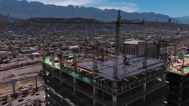 Cinematic 4K aerial drone orbits two high-rise buildings under construction with tower cranes in downtown Monterrey, Nuevo Leon, with workers visible and the city skyline in the background