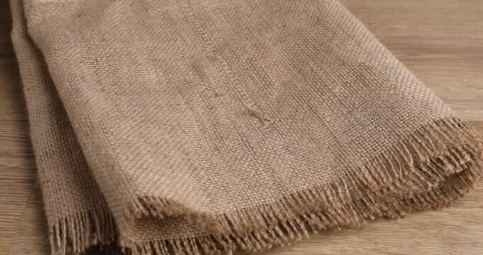 Woman putting folded burlap fabrics onto wooden table, closeup
