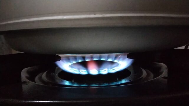 Close-up of a blue gas flame igniting on a stovetop burner, cooking preparation