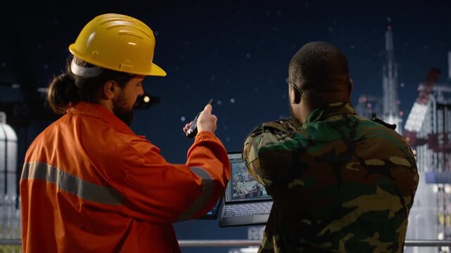 Drilling ship worker and military man use laptop to monitor infrastructure threats during war causing oil crisis while a soldier on offshore rig uses device to analyze conflict disruption.
