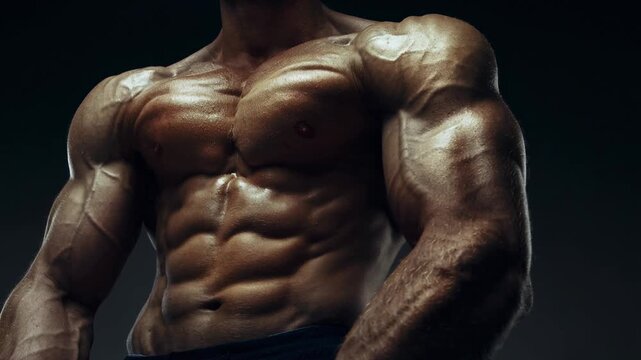 Close up of muscular man flexing glistening torso and arms fitness workout strength training