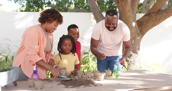 African American family filling pots at backyard table, mother scooping soil with blue trowel