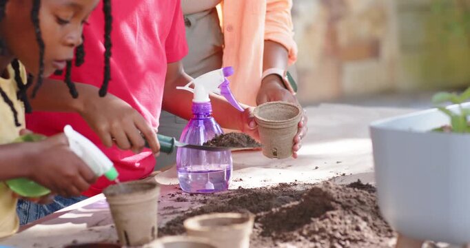African American mom guiding kids scooping soil from pile into biodegradable pots to plant on patio