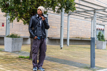 Adult male standing in plaza holding phone to face, wearing beanie and leather jacket, copy space © wavebreak3