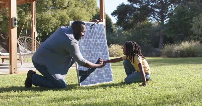 African American father positioning solar panel, teaching youth and guiding youth touching in yard