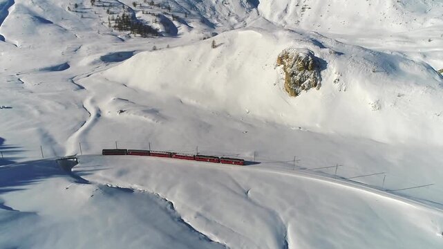 Aerial View of a Red Passenger Train Traveling Through a Breathtaking Snowy Mountain Landscape in Winter
