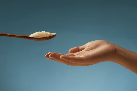Spoon of Uncooked Rice Above Open Hand on Blue Background