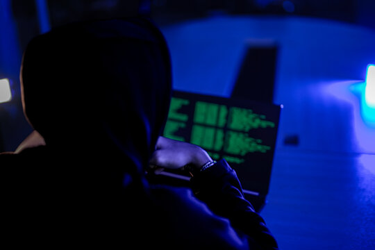 Hardworking software developer writing complex code on laptop at night. Freelance programmer working late on new digital project in modern dark blue workspace.