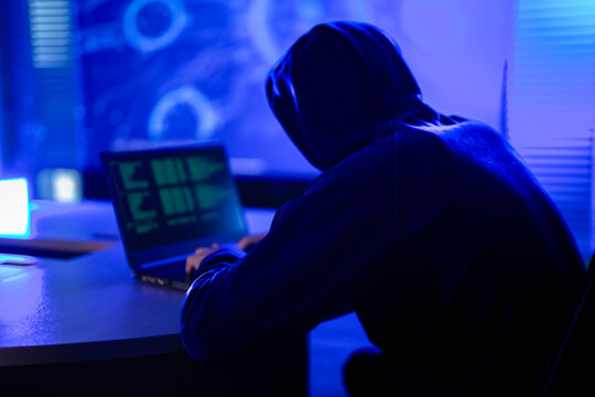 Hardworking software developer writing complex code on laptop at night. Freelance programmer working late on new digital project in modern dark blue workspace.