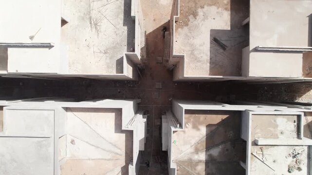 Top-down drone lift shot of a residential construction project, revealing the concrete structural layout of multi-unit buildings and adjacent highway infrastructure