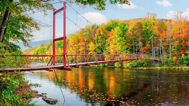 Red suspension bridge crossing a peaceful river surrounded by vibrant green nature landscape