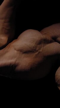 A male bodybuilder poses in shorts, showing off his arm muscles.