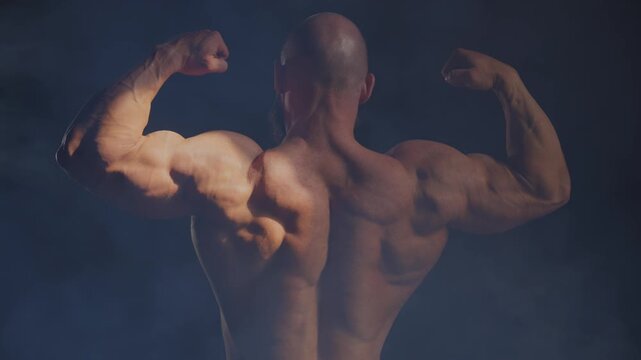 A male bodybuilder poses in shorts, showing off his back muscles.
