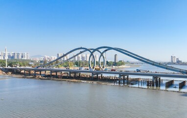 Naklejka premium Modern Blue Loop Bridge Over River with City Skyline