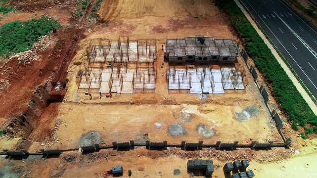 High-angle aerial drone reveal shot of a residential construction site, showing rebar foundation grids, concrete slab progress, and adjacent highway infrastructure